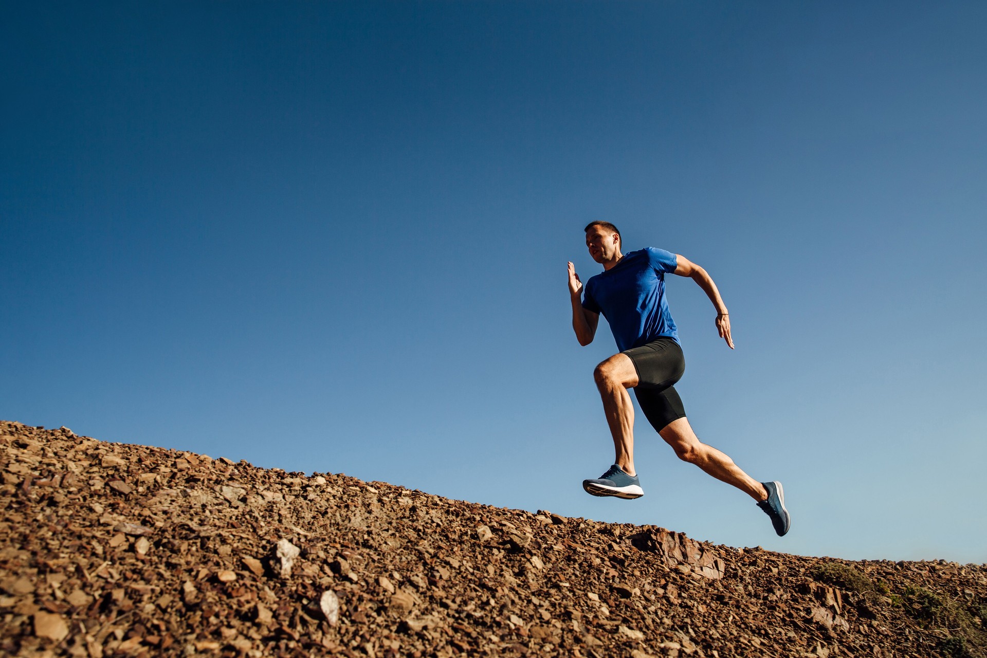 Low Angle View Of Man Jumping On Rock Against Clear Sky